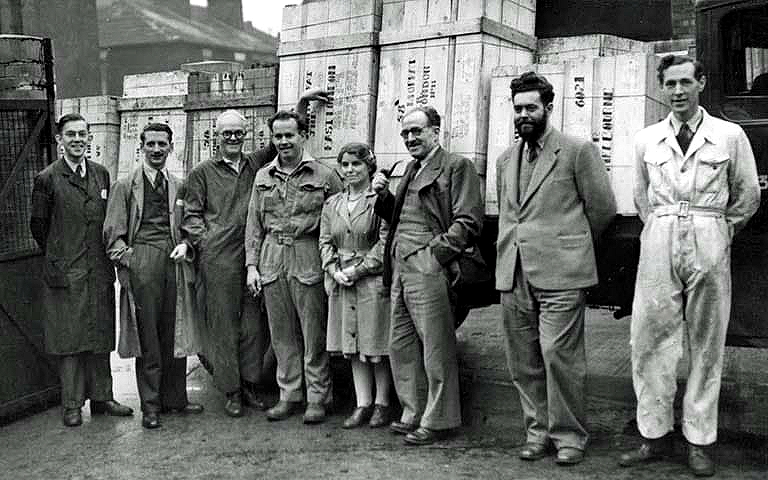 Eight members of the management team at Kingfisher Lubrication standing in a line in front of a lorry carrying their latest export in crates. Denys is the second figure from the right.